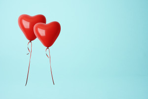 Two red heart shape balloons against blue background